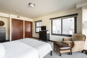 Cherry wood closet doors and dark wooden dresser with flat screen TV, large suede accent chair and large windows for natural light