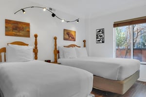 The two twin beds have crisp white linens, wood bedframes, and stylish art and lighting above the beds.