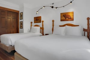 The two twin beds have crisp white linens, wood bedframes, and stylish art and lighting above the beds.
