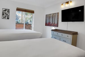 The second bedroom has two twin beds, dresser, and wall mounted TV above the dresser.