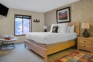 Park Station 122s main suite has a king bed with a wood frame and headboard, large picture above and colorful rug.