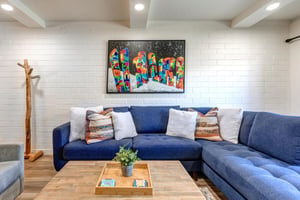 Park Station has a comfortable blue sectional sofa, with stylish throw pillows, wood coffee table, and snowboard art on wall.
