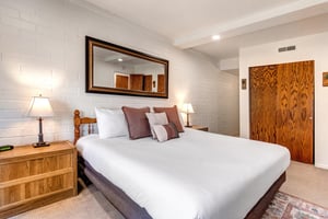 The main suite has a kingsize bed with crisp white linens and grey pillows, and wooden end tables and lamps.
