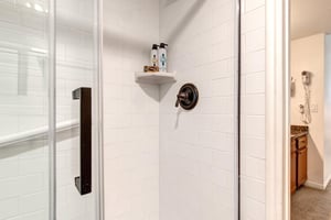 The en suite bathroom has a walk in shower with white tile, glass door, and black hardware.