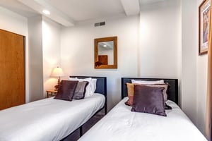 The second bedroom has two twin beds with white linens, grey throw pillow that matches a grey upholstered headboard.