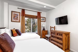 The second bedroom has two twin beds, wooden dresser, and flat screen TV mounted to the wall.
