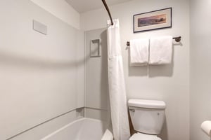 The shared bathroom has a white shower and bathtub surround with a white shower curtain and a white toilet.