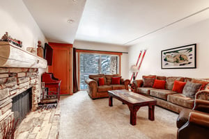 Park Station 134s living room with brown upholstered couches, red pillow, and large sliding glass doors with trees beyond.