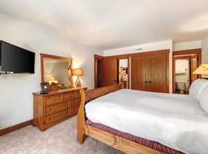 Park Station 134s main bedroom with king size bed, wooden dresser with light and mirror and wall mounted TV.