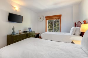 Park Station 134s second bedroom with two twin beds, white linens, dark wood dresser, wall mounted TV and window.