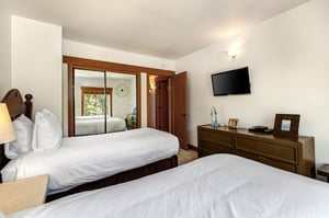 Park Station 134s second bedroom with two twin beds, mirrored closet doors, dark wood dresser, wall mounted TV and window.
