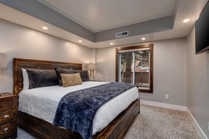 Warm light in the main bedroom with wooden bedframe, white linens and duvet and deep blue throw