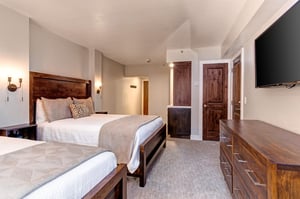 Guest bedroom sleeps 4 in two queen beds, wall mounted TV over the wooden dresser