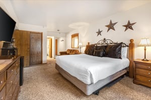 The main suite bedroom has a king size bed, white linens, wooden closet doors and love seat.