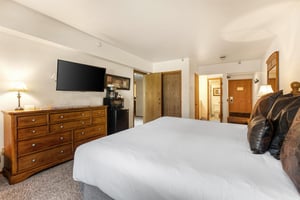 The main suite bedroom has a king size bed, white linens, wooden dresser and flat screen TV.