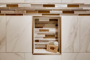 The shared bathroom has gorgeous white tile, with gold and brown decorative tile lining a shelf in the bathtub surround.