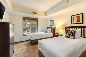 The second bedroom has two twin beds with white linens, wood bedframes, and fun animal print pillows to match.