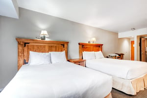 One of the bedrooms offer two queen beds with wooden furniture.