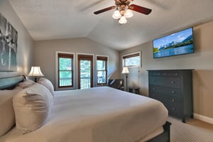 Main bedroom suite with wall mounted flat screen TV, dark wood dresser and black leather accent chair