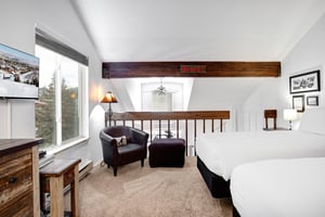 Unwind in your spacious bedroom featuring exposed wooden beams, comfortable seating area, and peaceful mountain views through the large windows.
