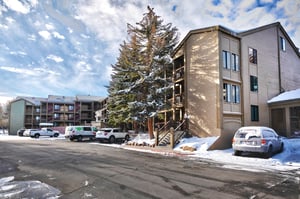 Winter exterior view of the property buildings with snowcovered evergreen trees and convenient parking available for guests.