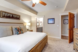 Sink into plush bedding and unwind beneath the ceiling fans gentle breeze. Your private ensuite bathroom awaits through the doorway, while artwork and warm wood tones create a cozy mountain retreat.