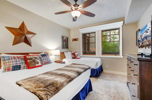 Unwind in this cozy bedroom with plush beds dressed in soft linens, warm rustic décor, and natural light streaming through windows that frame leafy views—your perfect retreat after a day of adventure.