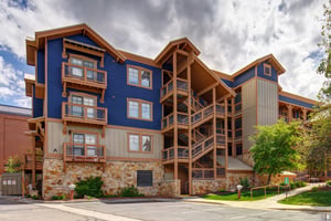 A striking mountainstyle property featuring bold blue siding, natural wood accents, and stone foundation set against dramatic skies—part of the welcoming arrival experience.
