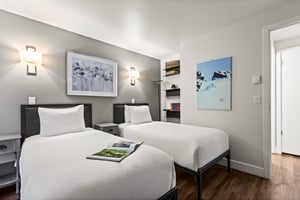 Bright guest bedroom with two twin beds, modern artwork, bedside tables and shelving with books