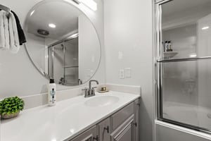 Secondary bathroom with spacious vanity, round mirror and tubshower combination with glass doors
