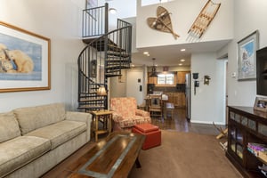 Open living room with sleeper sofa, spiral staircase, vaulted ceiling and dining area in the background