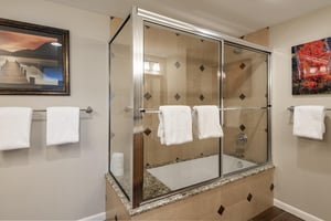Main bathroom with tiled tub and shower combination, glass enclosure and fresh white towels
