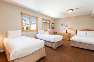 Spacious open loft sleeping area with three beds, wood furnishings and large windows with natural light