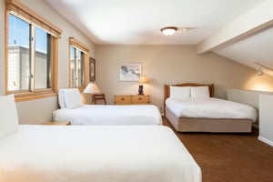 Open loft sleeping area with two twin beds, one queen bed, wood furnishings and large windows with natural light