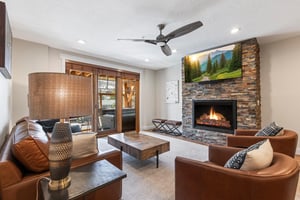 Beautifully designed living room with leather seating, stone fireplace, TV and doors opening to the outdoor patio.