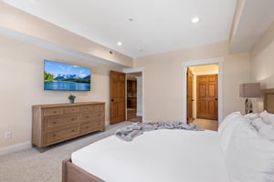 Spacious main bedroom with king bed, wallmounted TV, wood dresser and direct access to the ensuite bathroom.