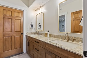 Ensuite main bathroom with spacious double vanity, granite countertop, wood cabinetry, large mirrors and modern lighting.