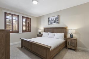 Spacious second main bedroom with wood king bed, matching nightstands, bedside lamps and windows with wood shutters.