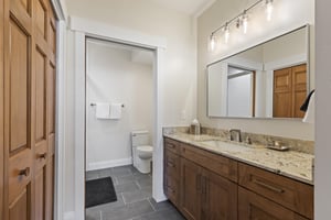 Ensuite bathroom with granite double vanity, wood cabinetry, large mirror, tile flooring and separate toilet area.