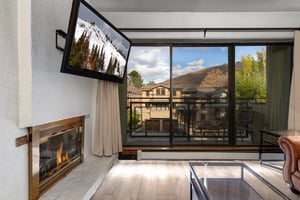 Living room with gas fireplace, wallmounted TV, large windows and sliding glass doors with mountain views.