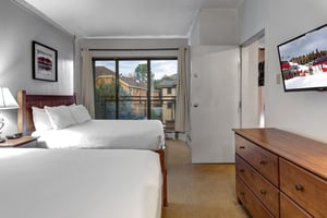 Bedroom with two queen beds, wood dresser and sliding glass door providing natural light and outdoor access.