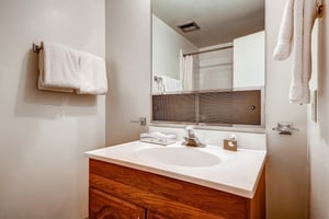 Full bathroom with spacious wood vanity, large countertop, mirror and showertub combination.