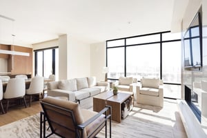 Stunningly bright living room with striking window walls, hardwood floors and large area rug, white couch, two white arm chairs, and leather and black metal accent chair.