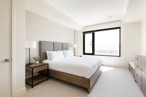 Main suite with luxurious king bed in white linens, platform wooden bed frame and high suede headboard, large picture window.