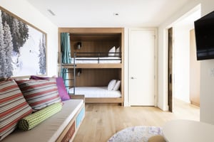 Twin bunk lounge room, built in bunk beds with privacy curtains and black security rail, lounging couch with colorful throw pillows and wall mounted TV.