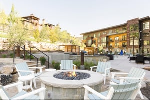 The Lift Condominiums outdoor circular firepit with white wooden Adirondack chairs, perfect for apres ski relaxation.