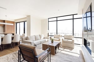 Stunningly bright living room with striking window walls, hardwood floors and large area rug, white couch, two white arm chairs, and leather and black metal accent chair.