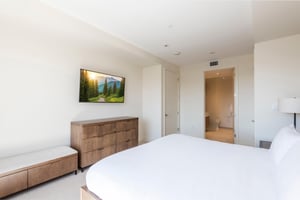 Spacious main bedroom suite with king bed, wooden dressers and woodsuede bench with wall mounted flat screen TV.