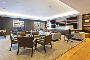 Hardwood and carpeted floor in the club room with various leather armchairs for seating and TVs and large sofa in the background.