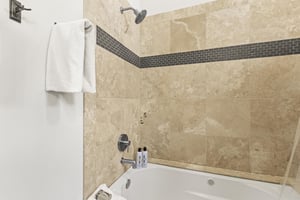 The shared bathroom has a white bathtub and cream tile surround with grey inlayed tile.